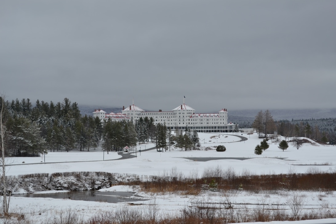 Stort hvidt hotelkompleks i et snedækket landskab med skov i baggrunden, som illustrerer omfanget af vintervedligeholdelse.
